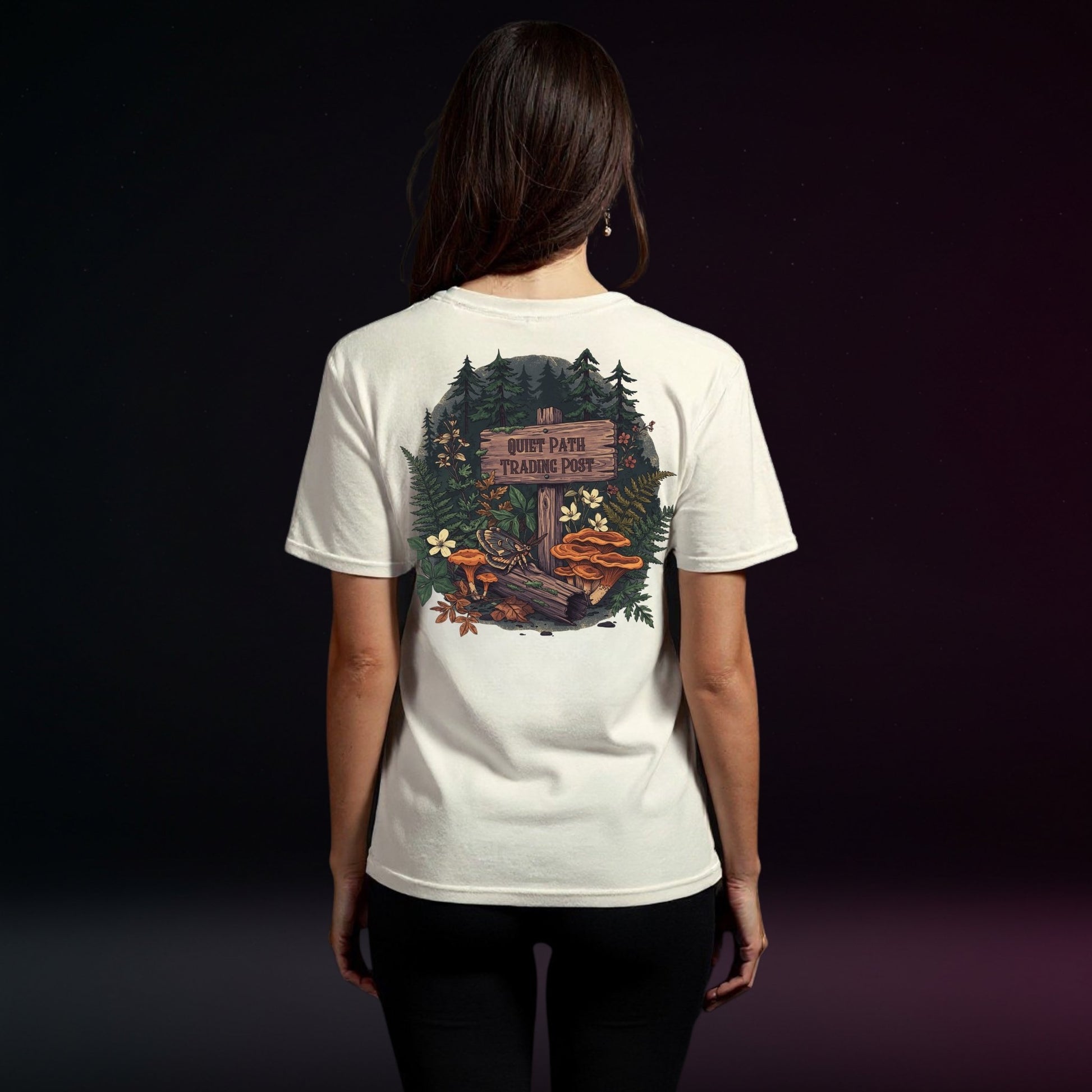 Person wearing a white t-shirt with a forest graphic on the back against a dark background