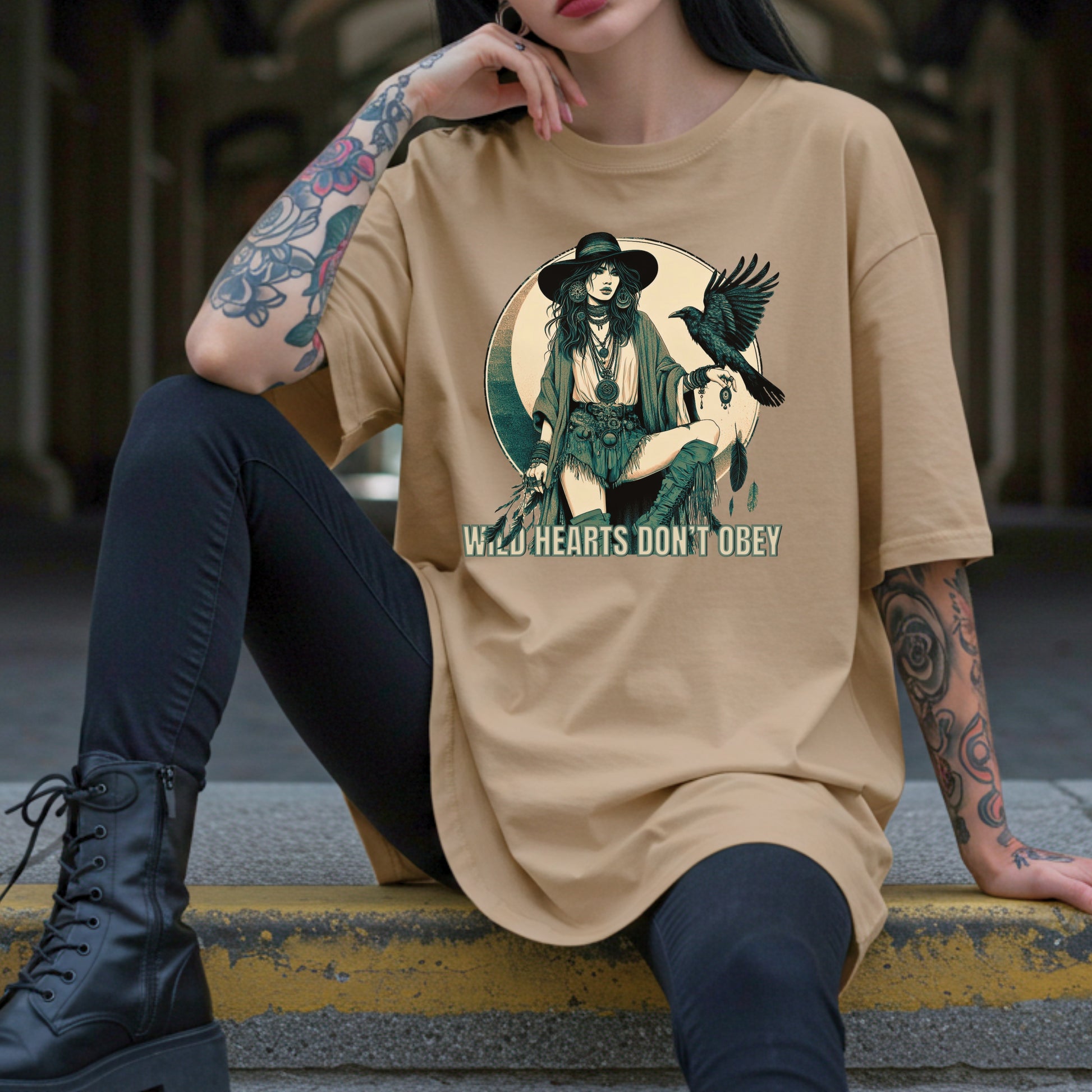 Person wearing a beige t-shirt with a graphic design and text, sitting on a ledge.