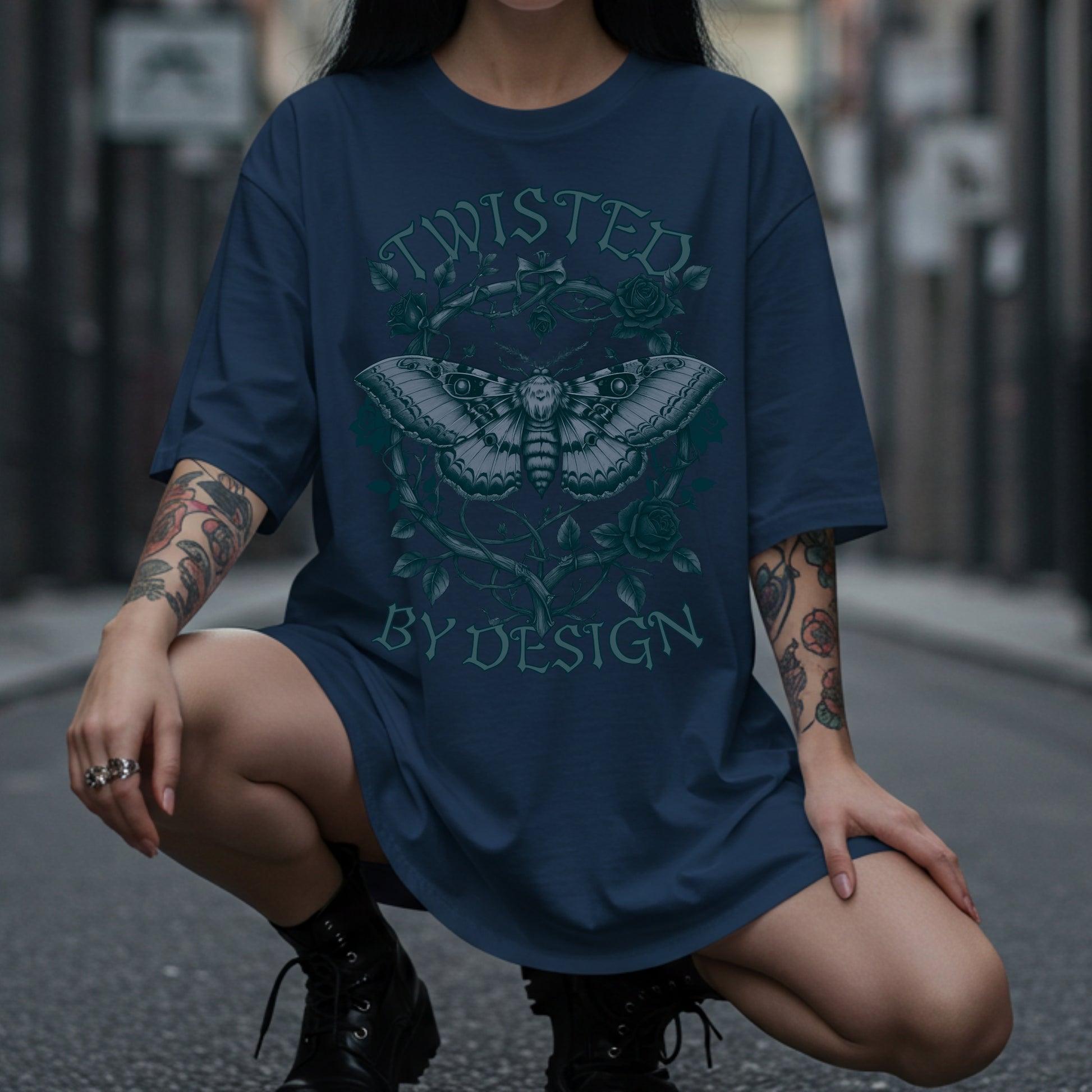 Person wearing a blue t-shirt with a graphic design and text, sitting on a street.